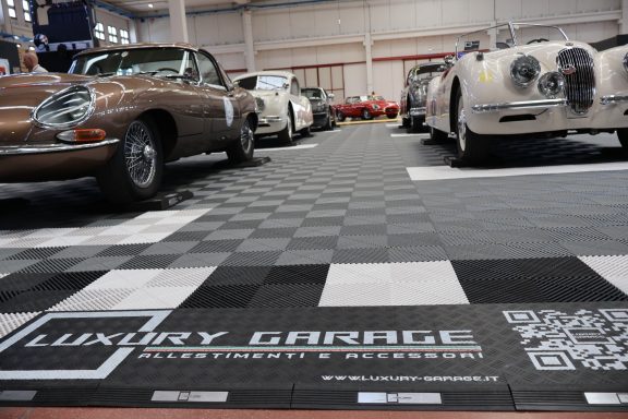Line of classic luxury cars displayed in a garage with a checkered floor.