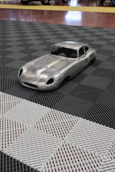 Modello in scala di un'auto da corsa argentata su un pavimento grigio a scacchi.
