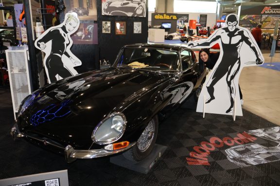 Auto sportivo nero esposto con figure stilizzate bianche sullo sfondo.