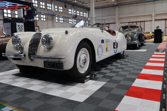 Vintage white sports car displayed in a spacious automotive exhibition hall.