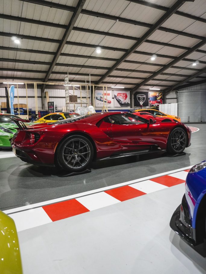 Cuscini Anti Ovalizzazione Pneumatici Rosso sports car parked in a spacious garage with various colorful vehicles.