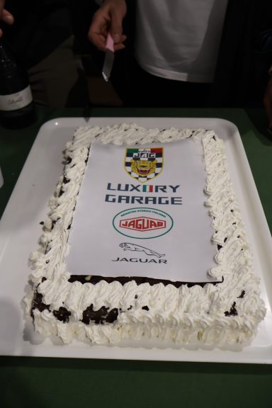 Torta decorata con panna, logo di un evento e una scritta.