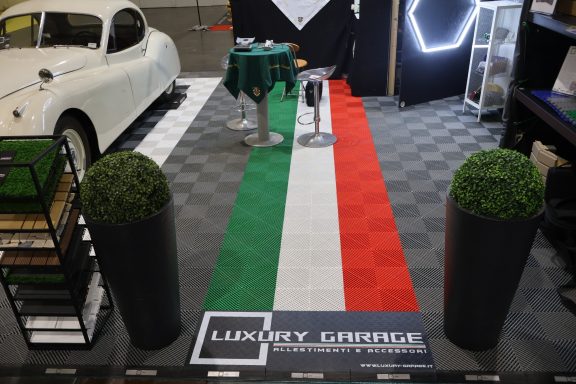 Stand featuring an Italian flag carpet, potted plants, and a vintage car in the background.