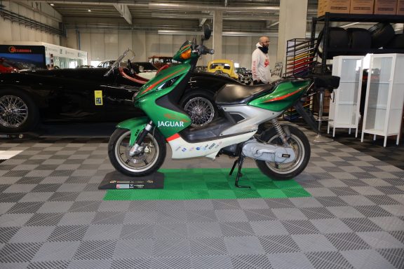 Moto sportiva verde e bianca su pavimento a scacchi, all'interno di un'area espositiva.