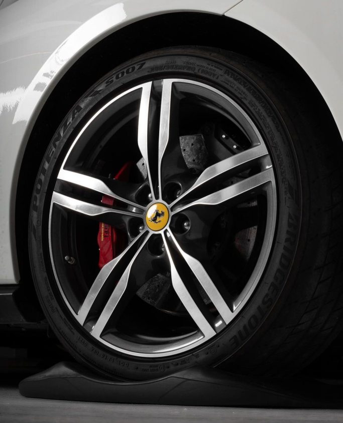 Sistema Anti Ovalizzazione per Pneumatici Rim of a luxury sports car featuring a sleek design and logo, dark alloy finish.