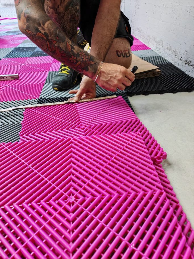 Posa Professionale Certificata Person laying pink interlocking tiles on a floor, using a measuring tool.