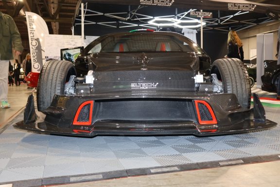 Auto da corsa con stile aerodinamico e grandi pneumatici posteriori, esposto su una superficie grigia.