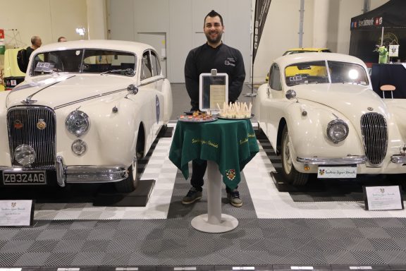 Due persone accanto a due auto d'epoca bianche in una mostra.