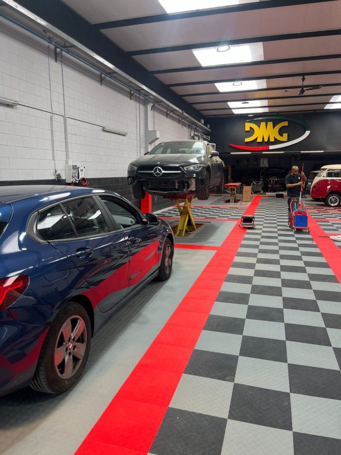 Auto workshop with a car on a lift, red and black checkered floor, and workspace in the background.