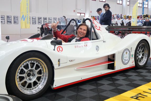 Pilota sorridente seduta in un'auto da corsa bianca su un pavimento a scacchi.