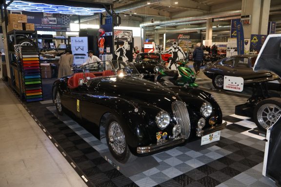 Classic black car displayed at an auto show among other vehicles.