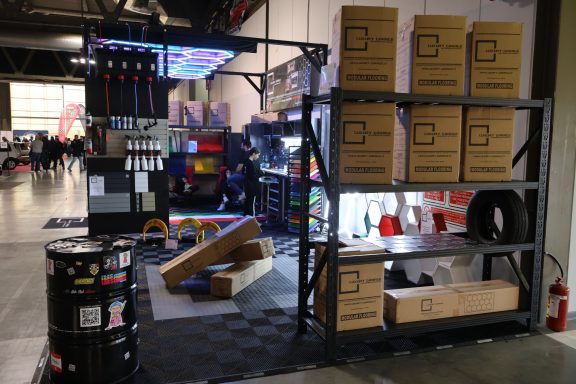 Stand with shelves of boxes, a colorful setup, and various equipment in a trade show environment.