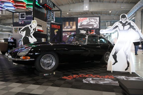 Auto d'epoca nera esposta con sagome di personaggi in un ambiente di esposizione.