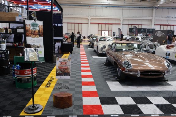 Auto show featuring classic cars with a checkerboard floor and exhibition stands.