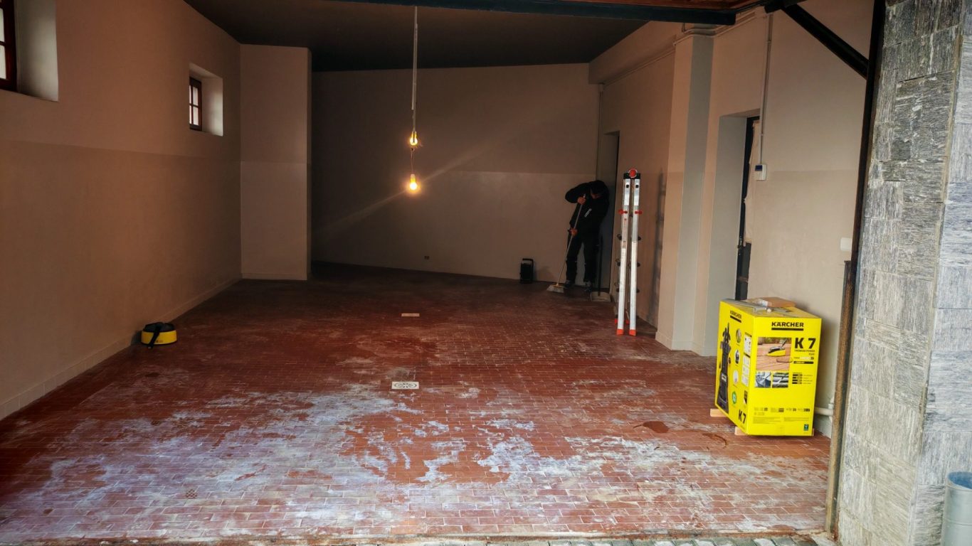 Spacious, empty room with red flooring, a worker, and two pendant lights.