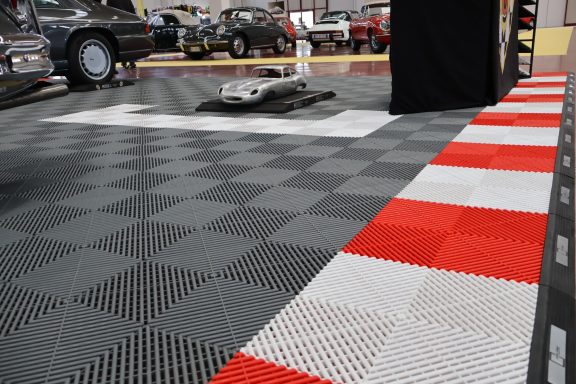 Paved floor with a checkerboard pattern in gray, red, and white; vehicles in background.