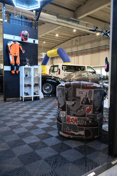 Spazio espositivo con abbigliamento, attrezzature e auto da corsa in mostra.