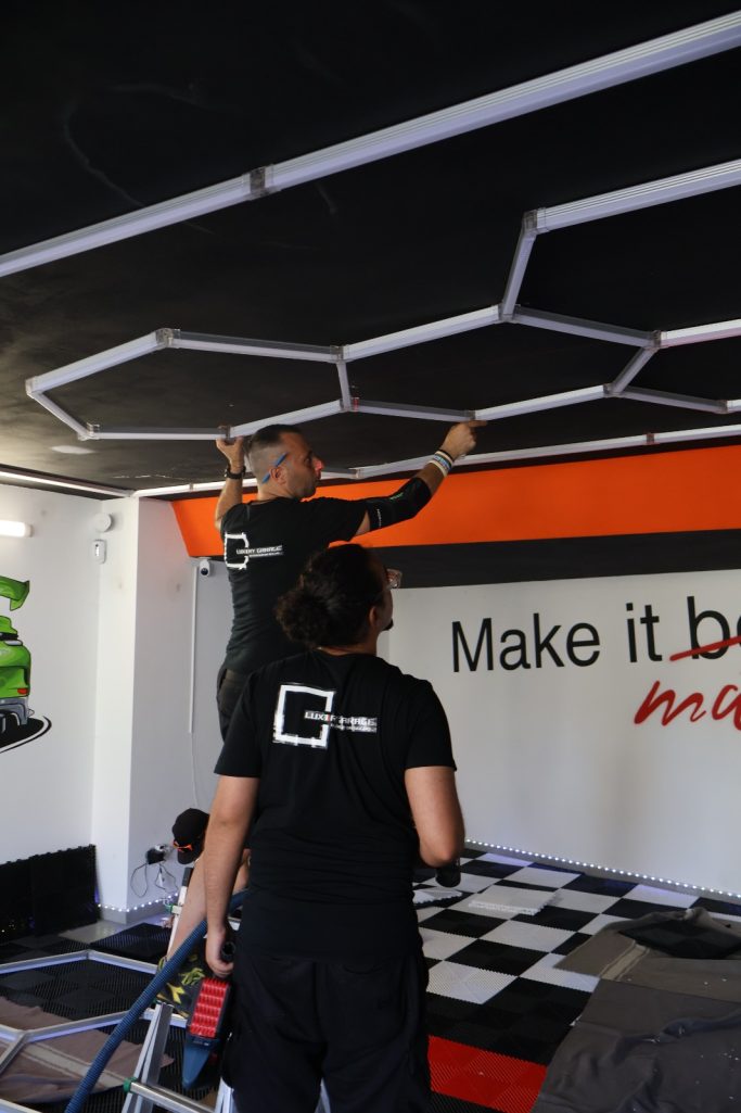 Installazione in Tutta Italia e Svizzera Two people installing a ceiling structure in a workspace with motivational text on the wall.