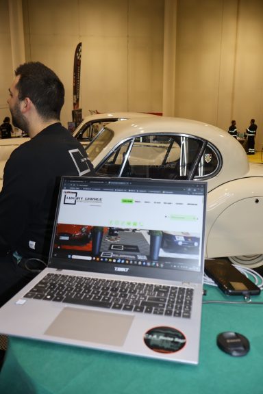 Laptop displaying a car-themed website, with a person and a vintage car in the background.