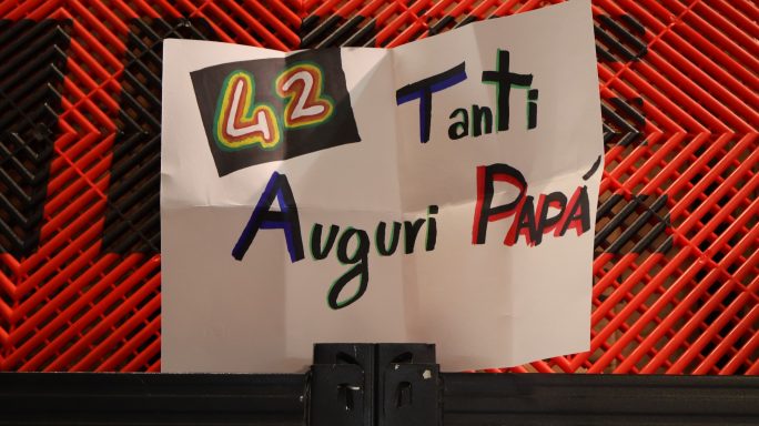 Cartello con scritto "Tanti Auguri Papà" e "42" su sfondo colorato.