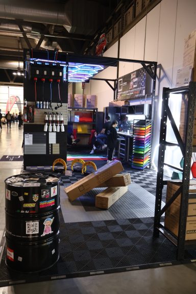 Spacious exhibition setup with colorful blocks, barrels, and a dark floor.