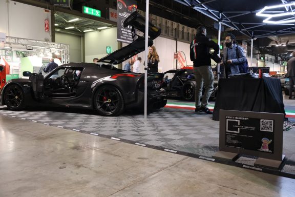 Sportscar displayed at an event with attendees and a checkered floor.