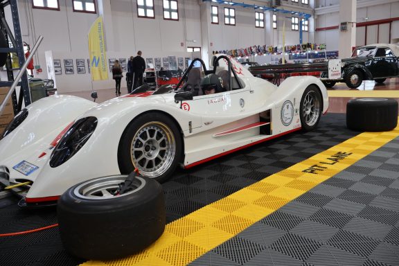 Racing car with a sleek design, parked on a checkered floor in a spacious indoor venue.