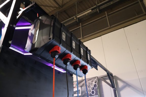 Struttura espositiva con cavi rossi e illuminazione viola, sospesa in un ambiente industriale.
