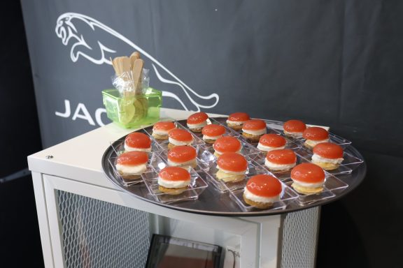 Vassoio con dolcetti decorati con glassa rossa su fondo nero con logo Jaguar.
