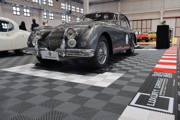 Vintage car displayed in a showroom with checkered flooring and various other cars in the background.