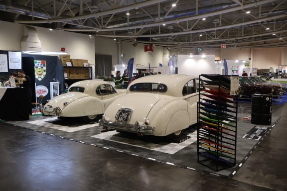 Duex vintage cars displayed in an exhibition hall with various banners and tools.