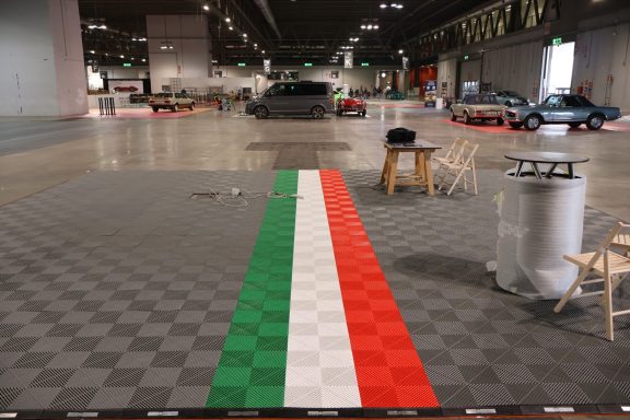 Pavimento con strisce verde, bianco e rosso, simile al tricolore italiano, in un'area espositiva.