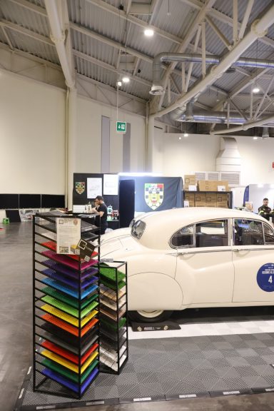 Classic white car near a display rack of colorful materials in a spacious indoor venue.
