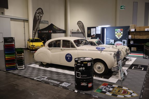 Due auto d'epoca esposte in un'area espositiva con barili e oggetti decorativi.