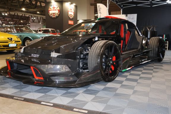 Auto da corsa nera con dettagli rossi e telaio esposto, esposto in fiera automobilistica.
