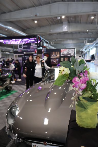 Due auto e donne in un ambiente fieristico, con fiori e decorazioni sul veicolo.